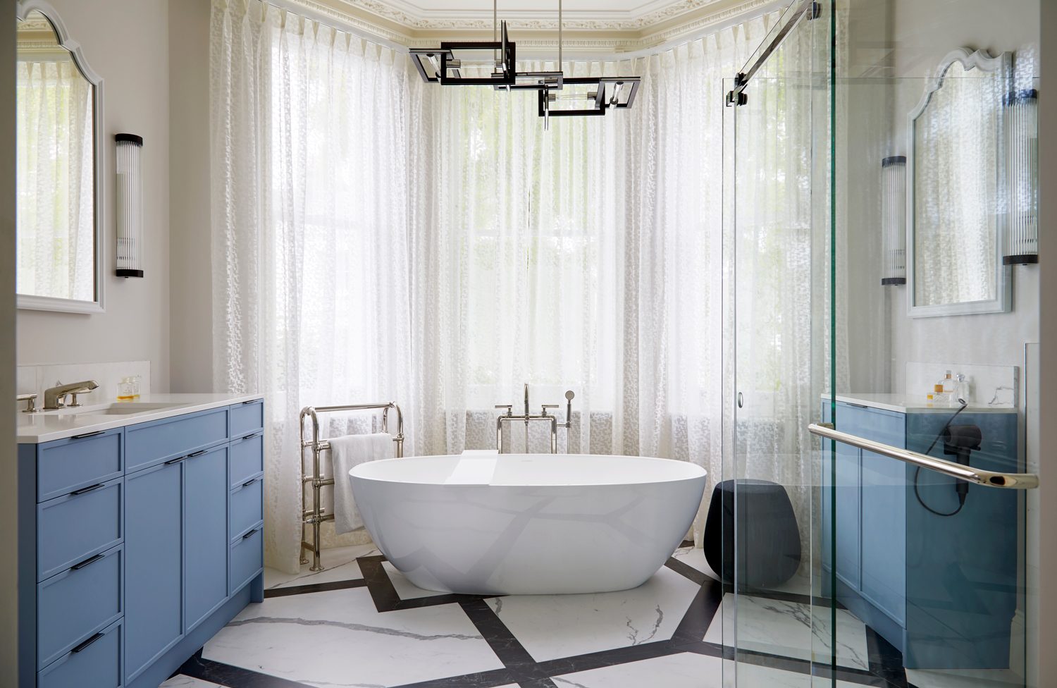 Luxury bathroom design with a freestanding bath in a bay window, twin blue vanity units and a black and white marble floor