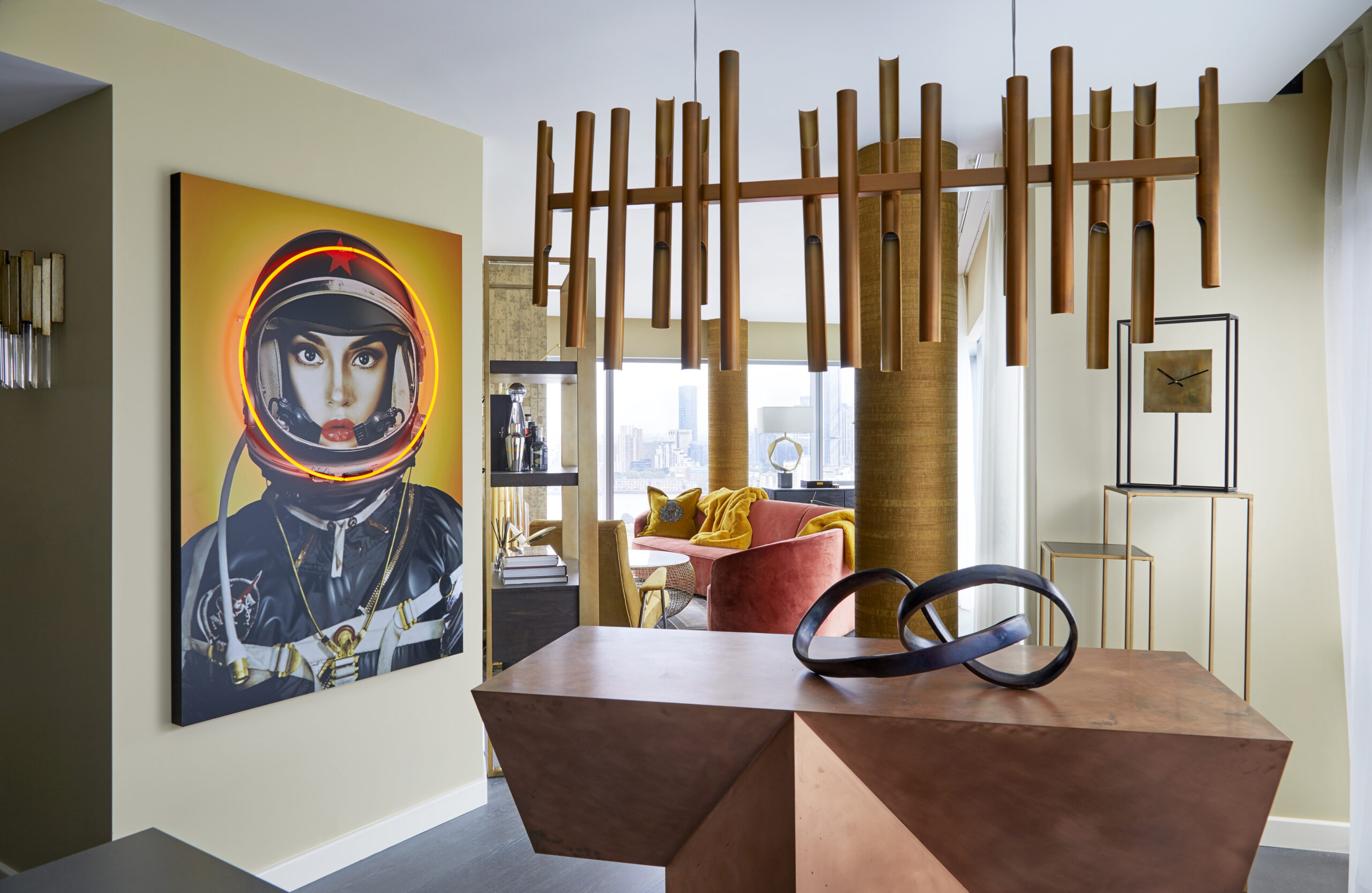 The dining area of the Greenwich Penthouse featuring a Flute Brass Long Chandelier from RV Astley, adding dramatic elegance, and a Space Girl Neon Artwork from Andrew Martin, bringing playful humour and urban cool to the room.