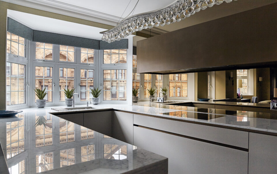 A meticulously designed kitchen in a luxury Knightsbridge apartment, showcasing bespoke elements and refined detailing. The space features hidden storage and smooth, rounded edges in adherence to the client’s preferences. Inspired by London’s grand public establishments and private clubs, the design combines the elegance of boutique hotels with personal touches, creating an atmosphere of understated grandeur. The open-plan layout seamlessly blends the kitchen with dining and lounge areas, embodying a sense of familial conviviality. This stunning space illustrates the principles of how to plan a kitchen with sophistication and functionality.